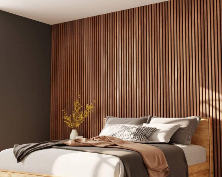 Modern bedroom with a vertical wooden slat wall behind a neatly made bed, gray bedding, and a beige-brown throw with a vase of yellow flowers on the nightstand.
