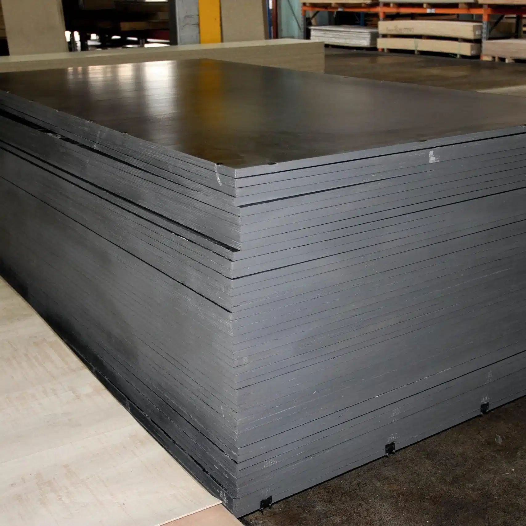 Stacked gray metal sheets in a warehouse, ready for shipment or storage with pallets in the background.