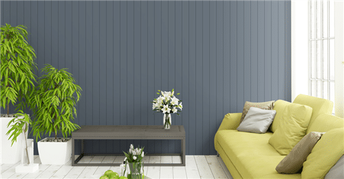 Living room with a blue paneled accent wall, a yellow sofa with cushions, a gray coffee table, and potted plants by a large window.
