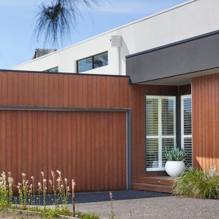 Modern house facade with vertical wooden siding, a window with blinds, and a white pot plant on a wooden step.