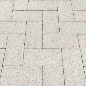 Light gray rectangular paving stones laid in an interlocking pattern on a sidewalk/driveway surface.
