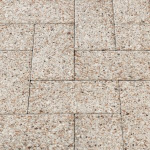 A paved surface of rectangular beige speckled stones with narrow grout lines arranged in a staggered pattern