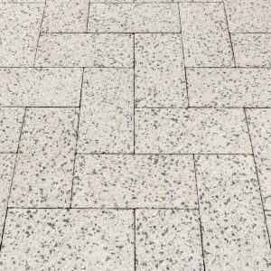 Light gray speckled concrete pavers arranged in a geometric, interlocking pattern forming a tiled walkway.