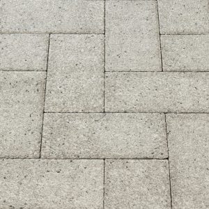 Close-up of light gray concrete paving stones forming an interlocking rectangular pattern, like a sidewalk surface.