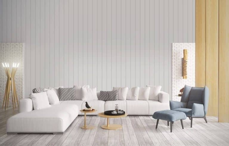 Modern living room with a white sectional sofa, two small round wooden coffee tables, and a blue armchair with ottoman in a bright, minimalist space.