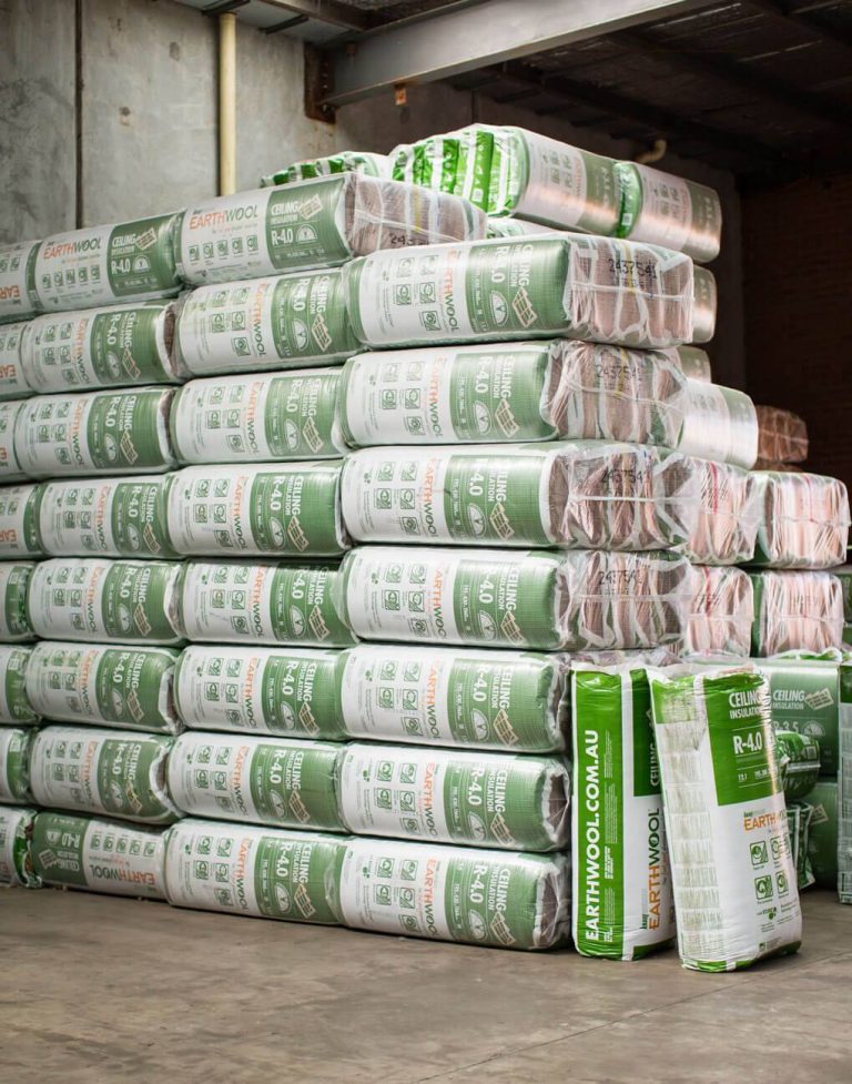 Stacks of EarthWool insulation bags piled in a warehouse, green-and-white packaging visible on pallets.